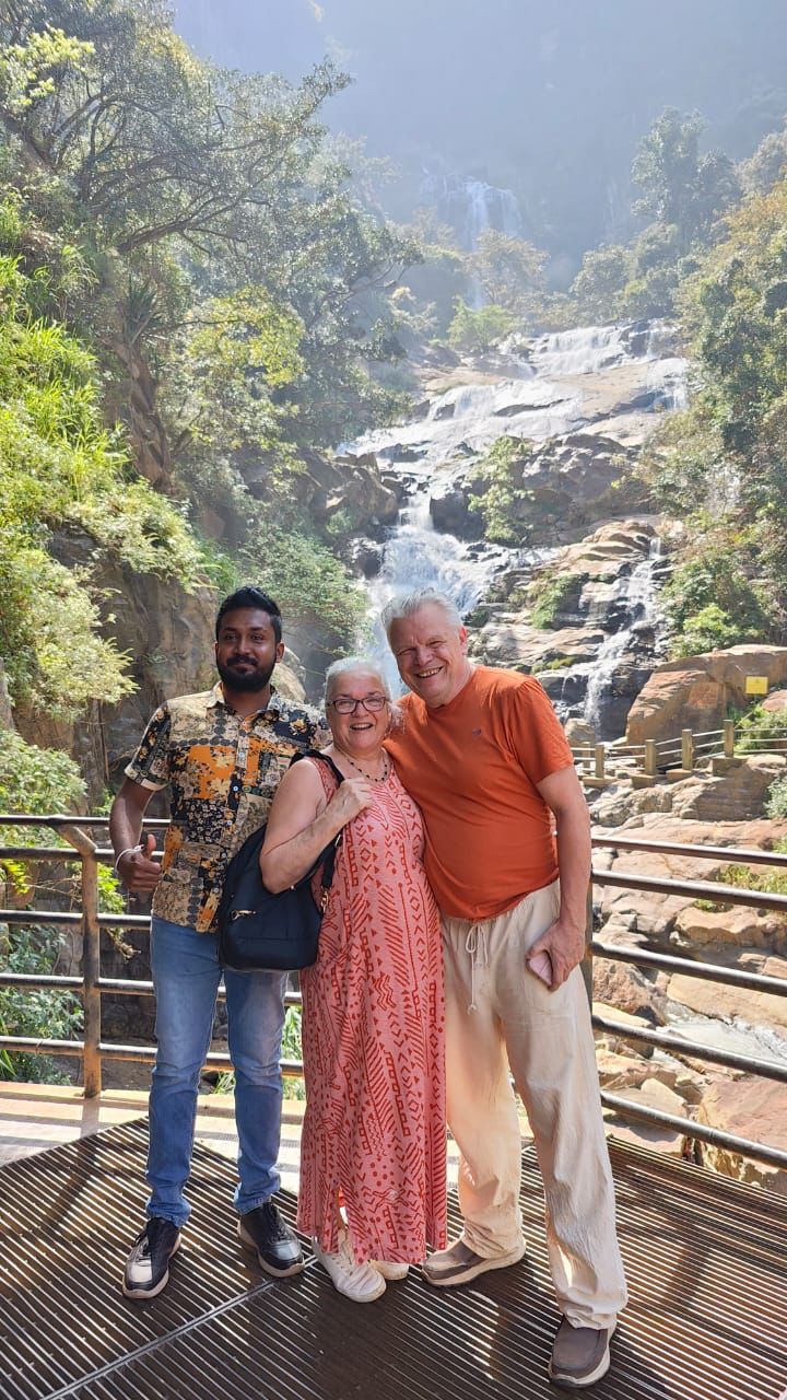 Two visitors standing beside a waterfall